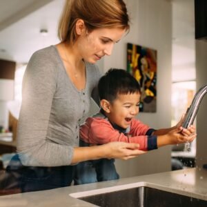 woman holds boy to wash hands at sink